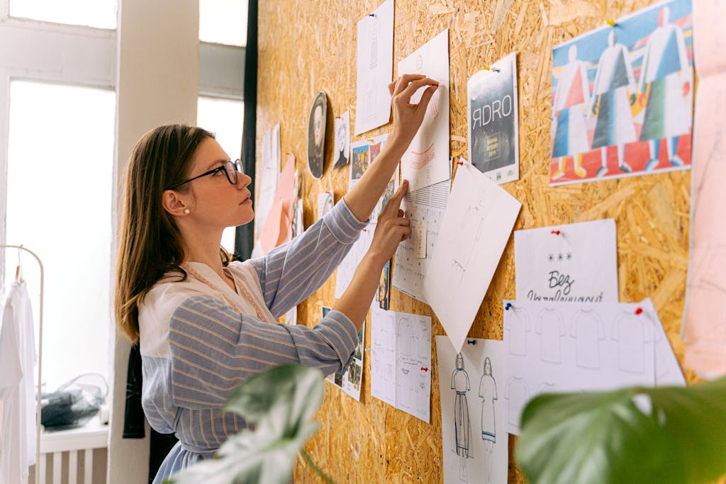 A woman fashion designer pinning sketches in a studio for inspiration.